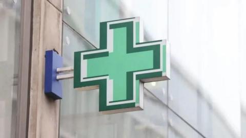 Green cross sign outside pharmacy window