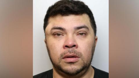 A custody image of Wesley Brito. He has short dark hair and dark stubble. There is a large lump above his right eye