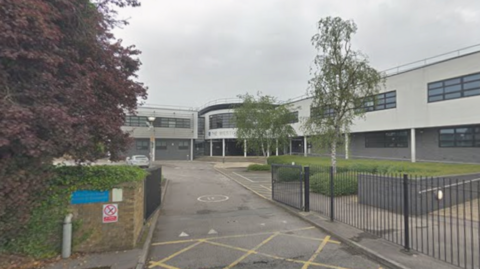 A general view picture of the school, a two-storey building with black gates surrounding it.