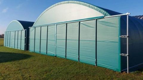 Light blue PVC hangars, akin to large industrial tents.