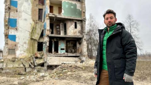 Newsround's Ricky Boleto stands next to a house which has been destroyed in the war in Ukraine
