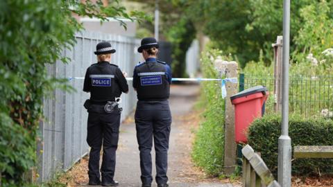 A police officer and a police community support officer stood at the scene of a stabbing in an alley in Chichester, West Sussex. The officers, both female, are looking down the alleyway behind police cordon.