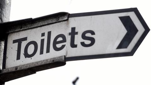 Sign high up against grey background saying toilets