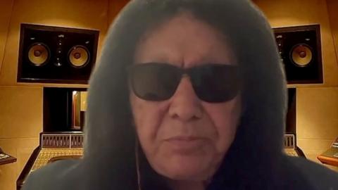 A close-up of Gene Simmons during a video interview. Behind him appears to be an image of a studio