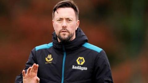 Ian Burchnall in a Wolves training top raises his right hand