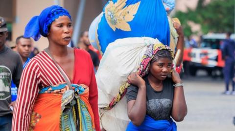 Two women carry their belongings