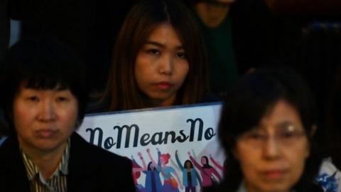 A woman holding a sign saying no means no