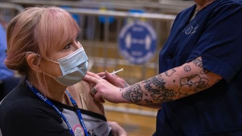 A nurse administers a vaccine to a fellow NHS worker