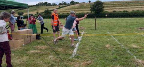 People lining up side by side throwing Dorset Knobs in a field, watched by spectators