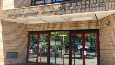 Cardiff Magistrates' Court, with glass doors leading into the building, and a sign reading Cardiff Magistrates' Courthouse in both Welsh and English above the doors 