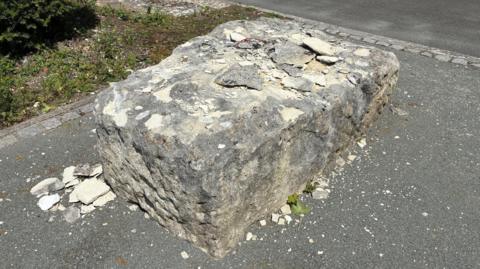 A large rectangular boulder on a path. Fragments of chipped rock are on top and next to it.