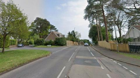 A Google street view of a main road, with roads on each side branching off into residential areas lined by wooden fences.