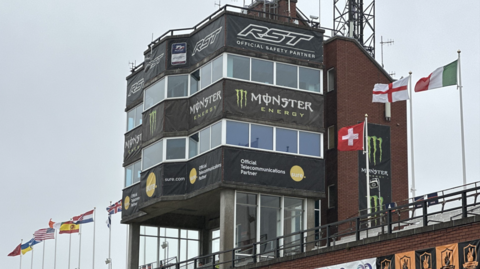 The tower at the grandstand in Douglas. The red brick building has large windows on each floor and the are international flags flying at either side.