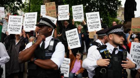 Police standing in front of protesters holding placards in support of Palestine Action