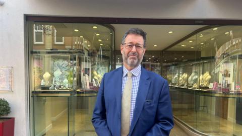 A man in a suit stood outside the front of a jewellery store