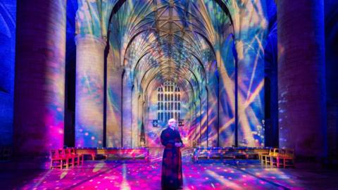 The Reverend Canon Nick Davies looking to the right of the camera with a colourful light display on the abbey around him.