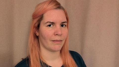 Woman in her thirties with long strawberry blonde hair and a pensive look on her face