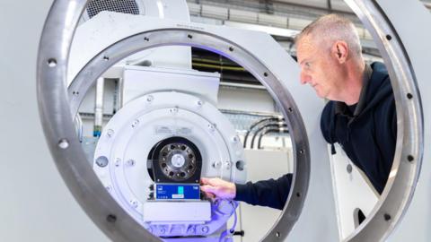 Image from inside a lab showing a man adjusting a part of a large piece of equipment made up of a series of large grey metal circles