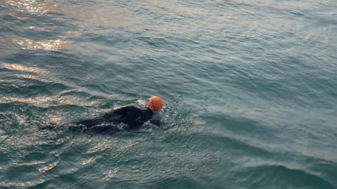 A man in a wetsuit, wearing an orange swimming cap 