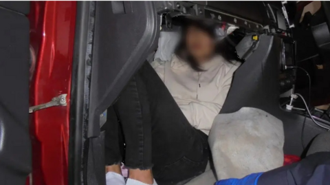A woman is half-sitting, half-lying down in a cramped vehicle compartment. Her face is blurred in the photograph, which has been released by the Home Office. She is wearing a white top and dark trousers.