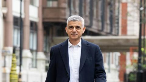 Sadiq Khan walking on street wearing suit with smile on face