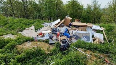 Fly-tipping - a large pile of waste dumped by grass and trees at a beautiful nature spot in Haworth, West Yorkshire