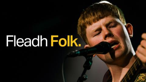 A boy strums a guitar while singing into a microphone
