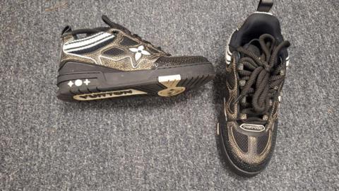 A air of black and gold trainers placed on the carpet.