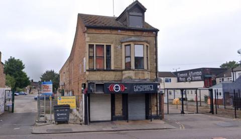 24B Lincoln Road, Peterborough, is a detached building with a black shop fornt. The shutters are down.