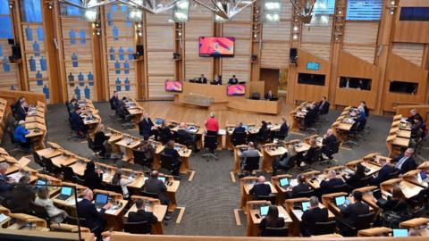 A general view of the Scottish Parliament chamber, with MSPs sitting at wooden desks 
