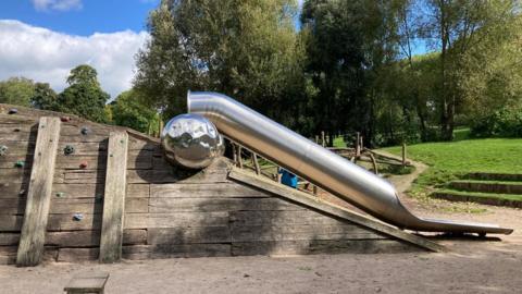 The slide at St George's Park. It includes a wooden climbing frame and a silver steel slide. 