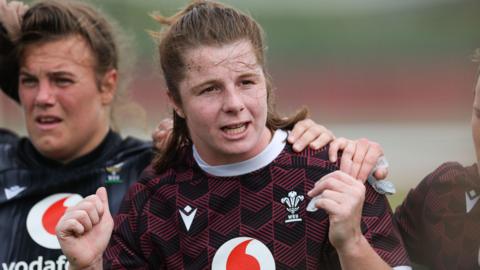 Kate Williams in a Welsh rugby training top offers instructions during a session. Her hands are raised as she makes a point. Carys Phillips' is to her right with her arm over Williams' shoulder.
