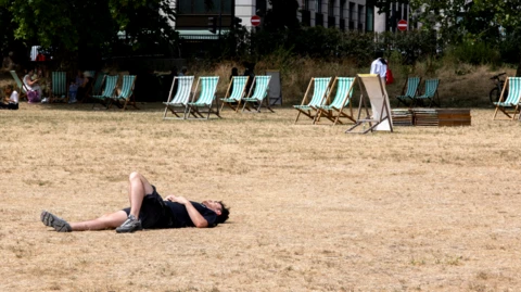 A man lying in a field of parched grass in the sunshine