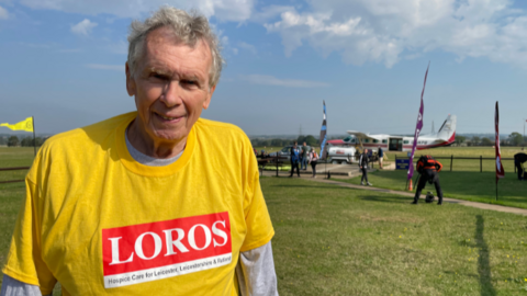 David Hartridge in a yellow T-shirt with a LOROS logo standing in from of the plane he jumped out of