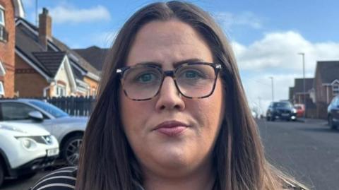 Julie Middleton looking straight down the camera. She is wearing glasses and has long dark brown hair. She's wearing a striped top.