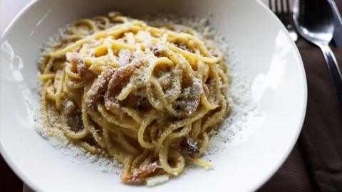 A bowl of pasta on a table next to cutlery.