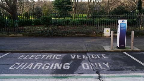 A sign on the road reads 'electric vehicle charging only' next to a charging point box