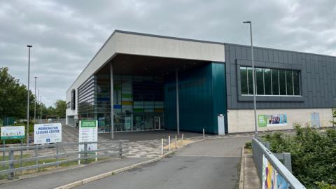 A general view of the leisure centre in Workington. The new building has dark cladding on one side and windows across the side where the main entrance is.