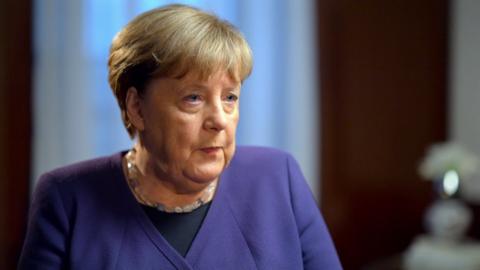 Angela Merkel. She is wearing a mauve top and necklace