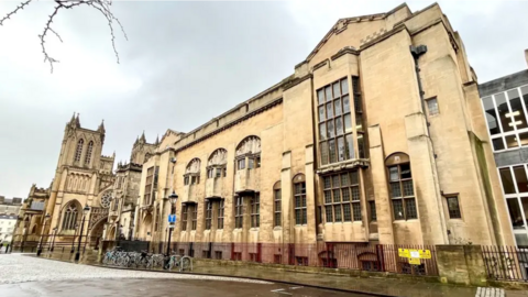 The exterior of Bristol Central Library. It is an Edwardian-style building with light yellow brickwork and there is a pavement and bike racks outside. 