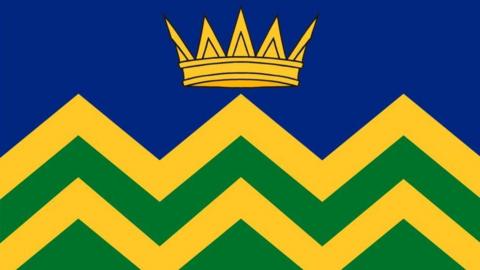 Graphic of a flag design showing a gold crown on a blue background above a yellow and green zig-zag pattern.