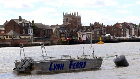 The King's Lynn ferry is a shallow grey boat with Lynn Ferry written across it. It is moored on the River Great Ouse. 