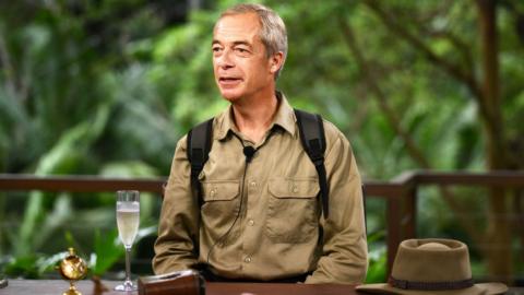 Nigel Farage sitting at a table being interviewed in the jungle