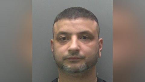 A custody image of Shazad Ahmed Shabir, who has a short beard.