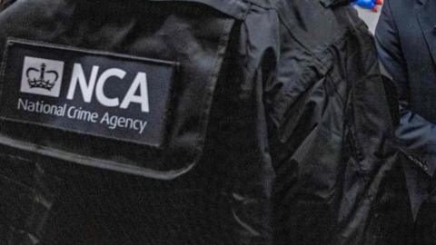 A black jacket with the letters NCA in white writing on the back and National Crime Agency underneath