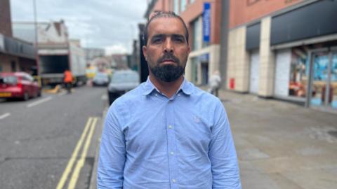 Man of Afghan origin in blue shirt short black hair stood on street