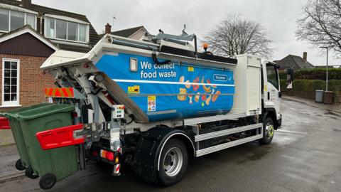 Image of a food waste collection truck on a street. It has "We collect Food waste" written as part of a sign on the side.