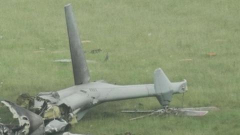 The tail of a grey military helicopter which has crashed in a field in Devon. Wreckage can be seen across parts of the grass.