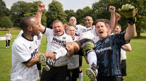 Millwall supporters involved in one of the EFL's club charity projects cheer and lift one of their team-mates