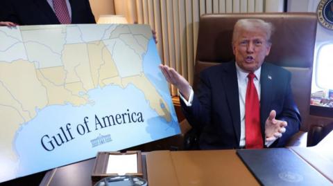 President Donald Trump gesticulates while sitting next to a poster that reads: "Gulf of America"